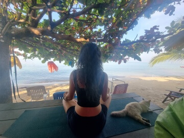 Meine Morgenroutine – Sandra Savanovic Sandra Savanovic meditiert am Meer auf Koh Samui, Thailand, während eine Katze neben ihr liegt.