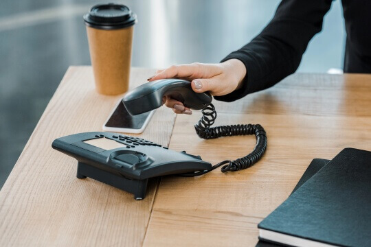 Kontaktaufnahme per Telefon Eine Frau greift zum Telefonhörer auf einem Schreibtisch.